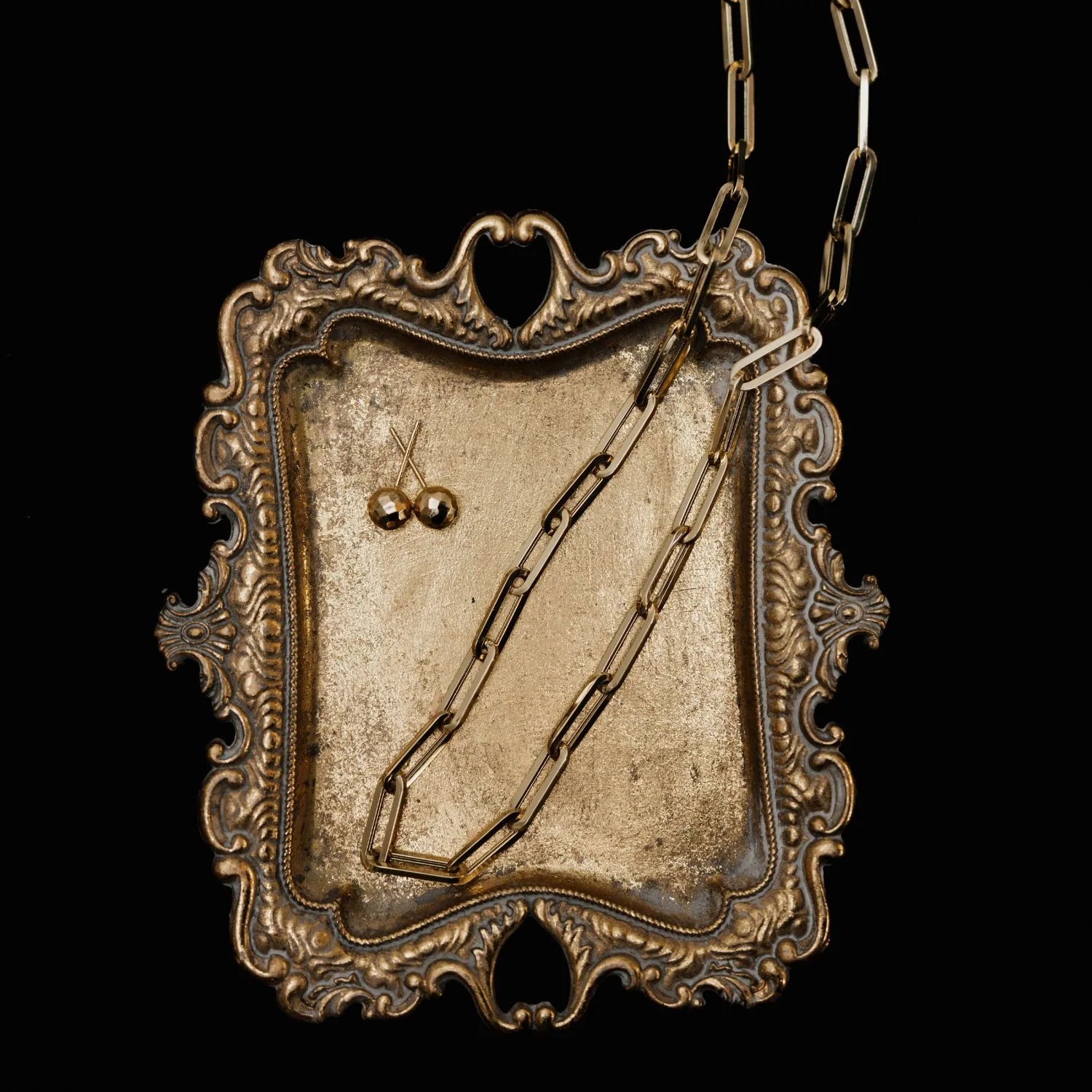 Gold paperclip chain necklace and stud earrings on an antique silver tray